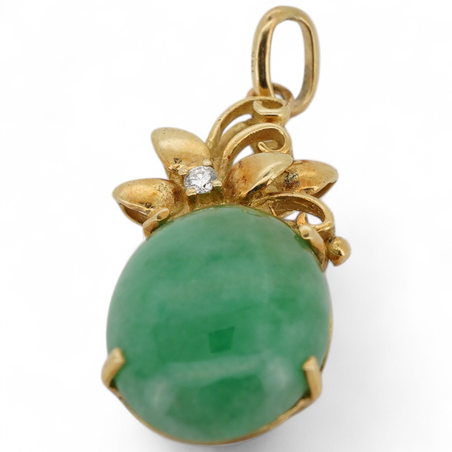 A jadeite and diamond pendant, the cabochon jadeite measuring approximately 14.8 x 11.8 x 4mm, to a foliate gold surmount accented with a brilliant-cut diamond weighing approximately 0.03 carats, mounted in gold, stamped
